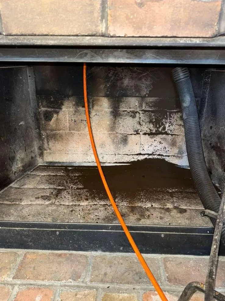 The inside of a brick firebox with soot-darkened walls, an orange sweep cable running down it and a vacuum hose at the right